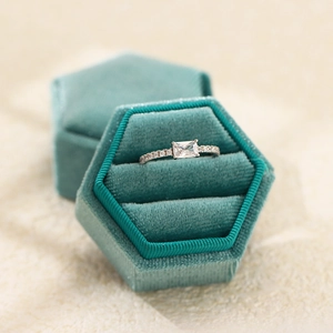 Elegant rectangular cut zircon ring in a green velvet box on a beige surface