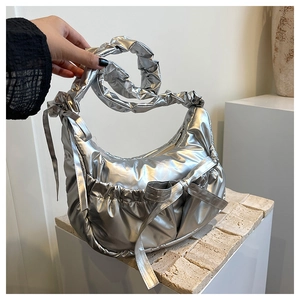 Detail of silver metallic puffy bag with bow accent and ruched cloud strap on white stand