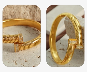 Detailed close-up of golden spiral cuff bracelet with crystal-paved ends on stone background