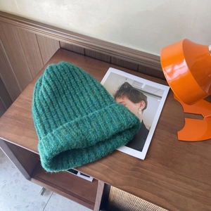 Detail of emerald green chunky knit beanie with ribbed texture on a wooden table