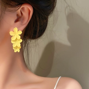 Detail view of a model wearing yellow matte floral drop earrings with a triple flower design