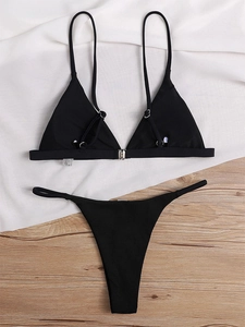 Detailed flat lay of black ribbed bikini set with silver front clasp on satin background