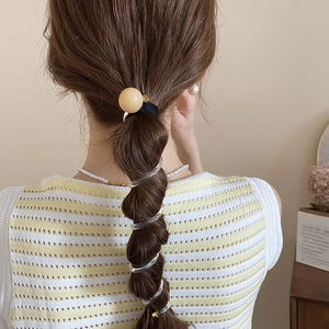 Détail d'un élastique spirale transparent avec une perle décorative de couleur jaune crème