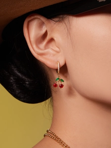 Détail de boucles d'oreilles cerise dorées avec cristaux rouges et verts sur un modèle