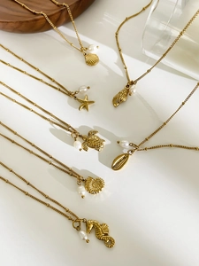Detail of gold ocean theme necklaces with starfish shell and pearl on white background