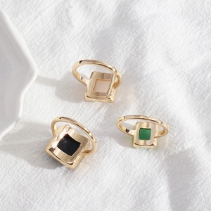Close-up of square geometric rings in cream, black, and green on white textured fabric