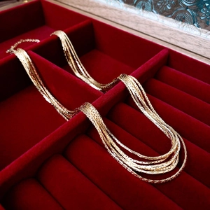 Detail of gold layered flat snake chains resting on a vintage red velvet jewelry tray
