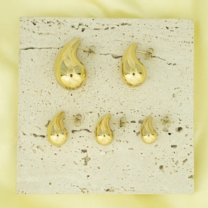Polished 18K gold teardrop stud earrings in five sizes on a travertine stone base