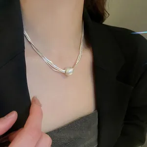 Multi-layer silver snake chain necklace featuring a large white pearl pendant on a model