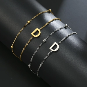 Detail of double-layer gold and silver chains featuring a polished letter D pendant
