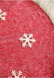 Macro detail of red Christmas tree skirt with white plush border and snowflake appliqué