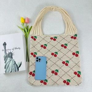 Flat lay of beige knitted cherry tote bag with a smartphone and tulips