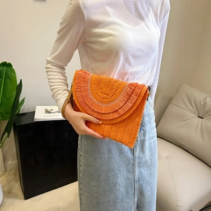 Detail of orange raffia woven clutch bag with fringe tassels held by a model
