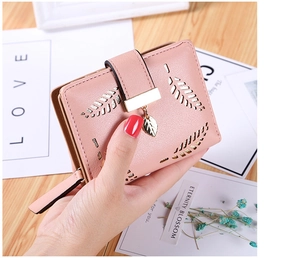 Close-up of pink leather wallet with leaf cutout detail and gold charm held by hand