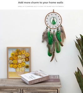 Close-up of bohemian dream catcher with emerald feathers and wooden beads on white wall