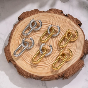 Three pairs of two-tone stainless steel hoop earrings on a rustic wood slice display