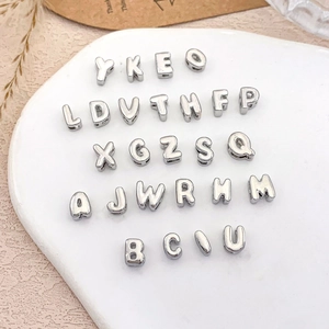 Detail of 26 silver metal alphabet pendants for DIY jewelry making on white board