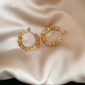 Macro shot of gold hoop earrings with irregular crushed texture on champagne silk fabric