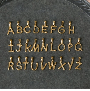 Full set of 26 gold bamboo style alphabet pendants from A to Z on dark stone texture