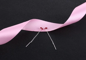 Detail of elegant silver tassel earrings with dark red zircon and pink silk ribbon