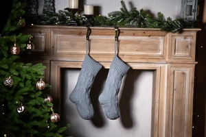 Close-up of grey knitted Christmas stockings hanging on a wooden fireplace with festive decor