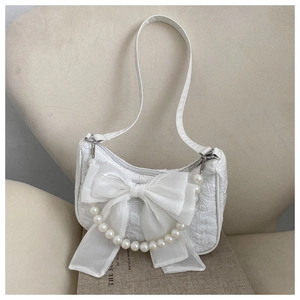 Close-up of white pleated handbag featuring an organza bow and pearl handle detail