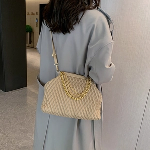 Beige quilted crossbody bag with gold chain strap shown on model in a modern lobby