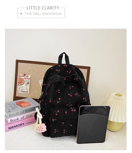 Close-up of black corduroy backpack with red cherry pattern and plush pendant