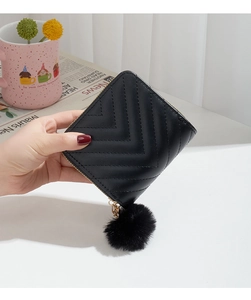 Close-up of black V-quilted wallet with golden zipper and fuzzy pom-pom charm detail