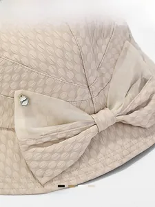 Detail of beige bucket hat featuring a mesh bow and silver forever charm pendant