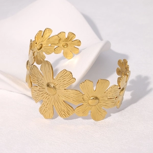 Elegant gold stainless steel daisy cuff bracelet on white fabric background