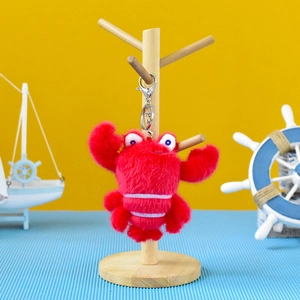 Detail view of a cute red plush lobster keychain hanging on a wooden display stand