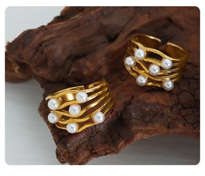 Detailed macro view of two gold wave-shaped rings with pearls on a natural wood block