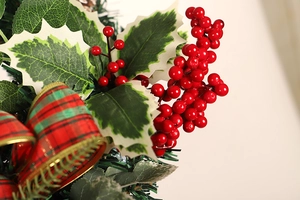 Close-up of artificial red berries and green pine needles with a plaid festive bow