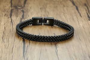 Macro shot of black plated stainless steel woven chain bracelet on a wooden surface