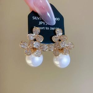 Close-up of gold floral pearl earrings with sparkling crystals and silver needles