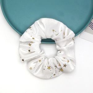 Close-up of white velvet scrunchie with golden star prints on a green tray