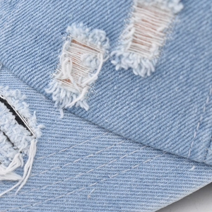 Detailed close-up of distressed denim baseball cap featuring torn edges and white stitching