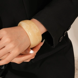 Detail of a wide resin bangle with cream marble texture worn with a black suit jacket