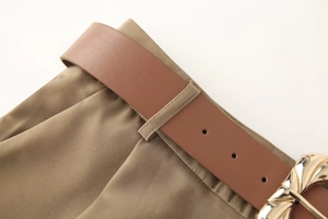 Vue macro détaillée du pantalon kaki avec ceinture en cuir marron et boucle dorée ondulée