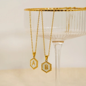 Detailed shot of hexagonal 18K gold letter A and B pendants on a glass rim