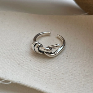 Detailed view of silver knot-shaped ring on textured linen fabric with soft lighting
