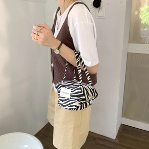 Detail of zebra pattern handbag with LOVE SOZAKKA label held by model in casual outfit