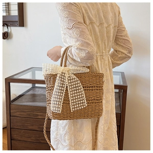 Detail of straw woven tote bag featuring a large white lace bow and matching straw strap