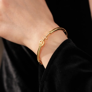 Macro detail of gold plated bangle with peace sign and rhinestone-set cross charm