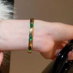 Detail of gold bangle featuring three green marquise-cut stones with polished finish
