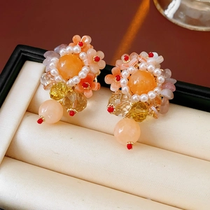 Vue détaillée de boucles d'oreilles fleurs avec pétales oranges, perles blanches et cristaux