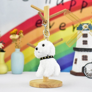 Cute white plush teddy dog keychain with gold star collar displayed on a wooden stand