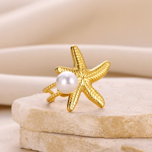 Close-up of a gold starfish earring with white pearl detail on a natural stone base