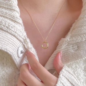 Close-up of minimalist gold hexagon pendant necklace worn with a white knit cardigan
